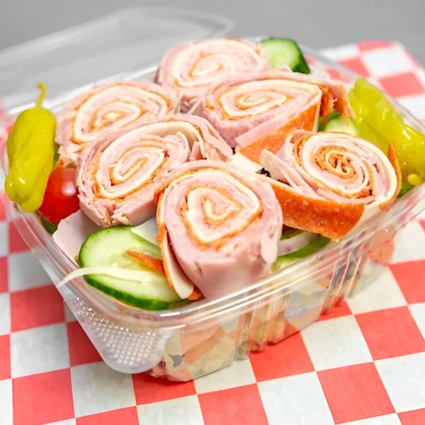 A clear plastic container of Checkers Pizza antipasto salad with rolled meats, vegetables, and peppers.