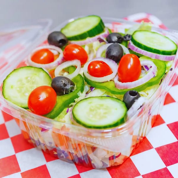 Fresh garden salad with cucumbers, tomatoes, olives, and onions in a clear plastic container.